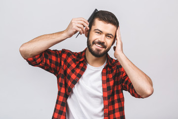 Neat, trendy, experienced, stylish, brunet, positive man looking at camera, combing, fixing, correcting his hair with hairbrush, holding hand on head, isolated on white background.