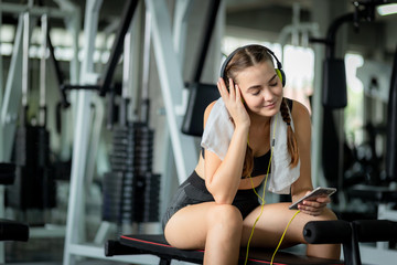 Fototapeta na wymiar Young attractive woman caucasian sitting and listening to music by earphones connect to smart phone. Relaxation after hard workout in gym. Fitness concept, Healthy, Sport, Lifestyle