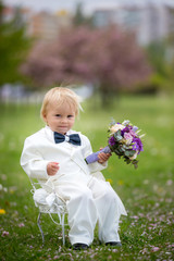 Beautiful toddler boy, dressed in white tuxedo, holding gorgeous flower bouquet for mothers day