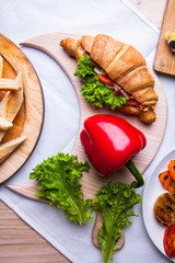 Top view of Homemade easy breakfast with fresh croissants, ham, red pepper and cheese on sandwich, tomato juice and cup of latte hot coffee on a wooden table.