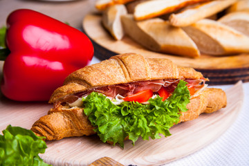 Top view of Homemade easy breakfast with fresh croissants, ham, red pepper and cheese on sandwich, tomato juice and cup of latte hot coffee on a wooden table.