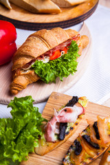 Top view of Homemade easy breakfast with fresh croissants, ham, red pepper and cheese on sandwich, tomato juice and cup of latte hot coffee on a wooden table.
