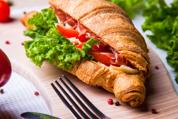 Top view of Homemade easy breakfast with fresh croissants, ham, red pepper and cheese on sandwich, tomato juice and cup of latte hot coffee on a wooden table.