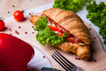 Top view of Homemade easy breakfast with fresh croissants, ham, red pepper and cheese on sandwich, tomato juice and cup of latte hot coffee on a wooden table.