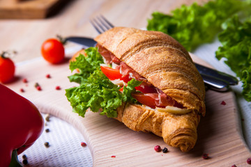 Top view of Homemade easy breakfast with fresh croissants, ham, red pepper and cheese on sandwich, tomato juice and cup of latte hot coffee on a wooden table.
