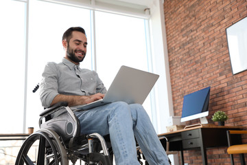 Young man in wheelchair using laptop at office