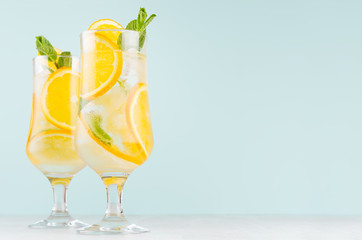 Homemade oranges lemonades with slices, ice cubes, mint in wet wineglasses on elegant blue color background, copy space.