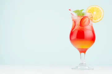 Foto op Plexiglas Fresh tropical red, yellow cocktail sunrise with slice orange, strawberry, ice, mint in misted wineglass on white wood table, blue  wall. © finepoints