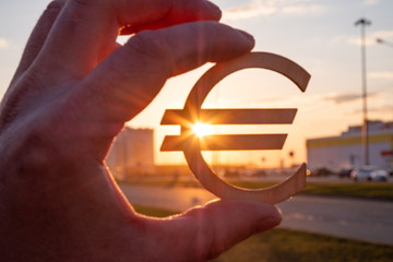 A hand is holding a euro sign made of wood on the background of the rays of the sun. wooden dollar sign in the sun