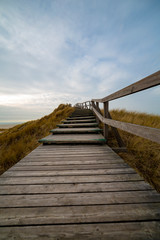 Fototapeta premium Wooden path with stairs or boardwalk leading through dunes to the top of a hill.