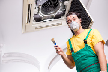 Young repairman repairing ceiling air conditioning unit 