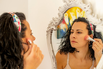 Beautiful woman applying blusher ( make up ) to her face at a mirror reflection