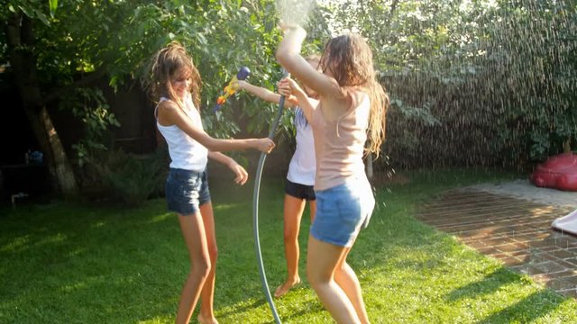 Slow motion video of cheerful teenage girls dancing and jumping with garden hose on hot summer day