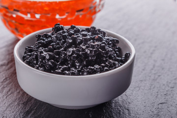 Fototapeta na wymiar red and black caviar in a bowl on a dark stone background