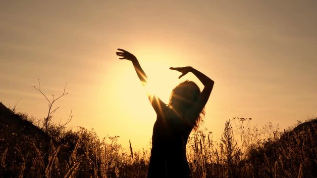Silhouette of a girl who dances and waves her hands at sunset in the open air. Close up. 4K.
