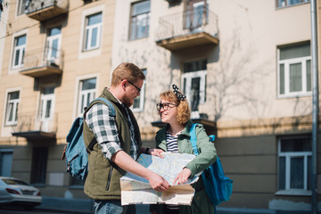 A young couple of tourists are looking for a road with a map in their hands in the city.