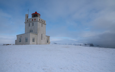 Panoramic image of the lighthouse of Cape Dyrholaey with snow and early morning light, winter in Iceland