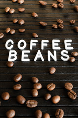 White lettering coffee beans and coffee seeds on black background under tilt.