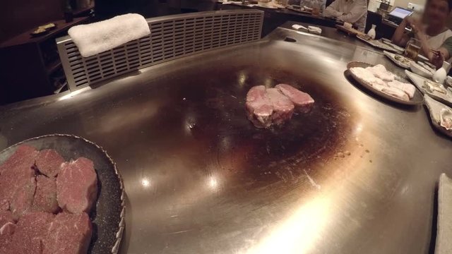 Chef Prepares And Serves Steak At Teppanyaki Restaurant On Hibachi. Sizzling Steak On Hot Plate Sizzling And Steaming While Cooked And Sliced And Plated. Guests Eating Traditional Japanese Cuisine.