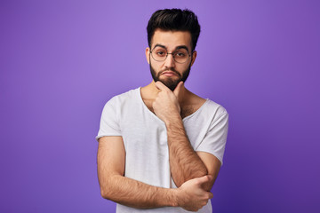 Pensive handsome guy keeps hand on chin, looks thoghtfully at the camera, thinks about information....