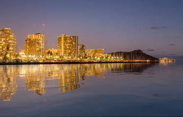 Panorama of the nightime skyline of Honolulu and Waikiki from Ala Moana park after the sun sets with artificial water reflection