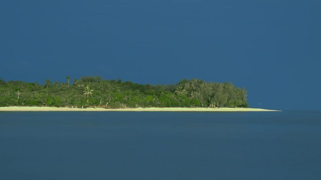 Tropical island on a sunny day with dark sea and cloudy blue sky