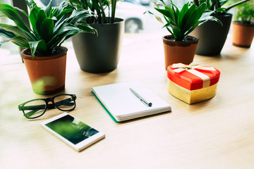 Top view photo of Smartphone, blank notebook, glasses, houseplants  and gift box on wooden table