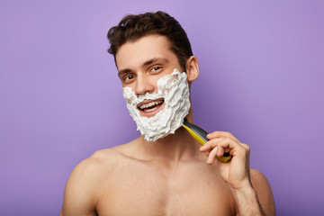 Headshot of satisfied cheerful attractive man grins at camera during shaving the beard, facial...