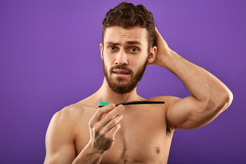 Obraz premium attractive man scratching his head and holding a brush. close up portrait. to brush teeth or not to brush, this is the question