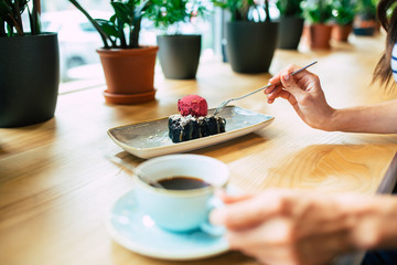 Smiling young Woman eating chocolate cake with berry ice-cream and cup of coffee in cafe