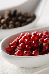 Pink or rose brazilian red peppercorns (schinus terebinthifolius) in white spoon on rustic white wooden table background