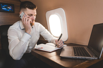 Young attractive and successful businessman talking on the phone and working while sitting in the chair of his private business plane