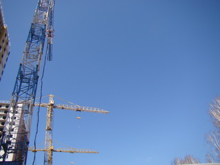 Construction cranes erect tall buildings. The clear sky is a space for text.