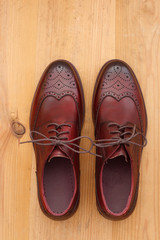 A pair of burgundy men's dress shoes wingtip brogue leather oxford view from above on brown wood background