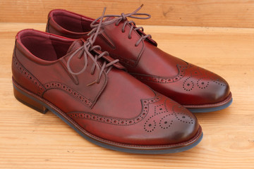 A pair of burgundy men's dress shoes wingtip brogue leather oxford view from above on brown wood background