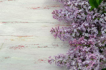 Frame of purple lilac and leaves on wooden background. Spring flowers. Decorative border, copy space, top view.