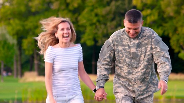 Soldier on a date with a girl, happy couple. Front view man in camoubackgrounde in the park walking with wife together.