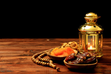 Islamic festival of Ramadan concept. Delicious tropical dates, dried figs, dried apricots on bamboo plates, rosary beads with a lantern on a pine wooden table background. Traditional Middle East cultu