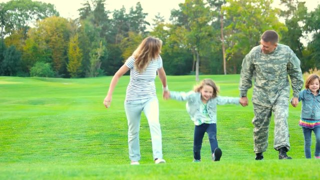 Family walking on the grass, holding hands. Four family members with father in military uniform going forward on the lawn.