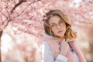 A Model looking at camera, posing in street, near blooming flowers. Female fashion concept