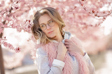 A Model looking at camera, posing in street, near blooming flowers. Female fashion concept