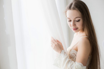 Attractive young seminude girl in night clothes posing sexually by the window