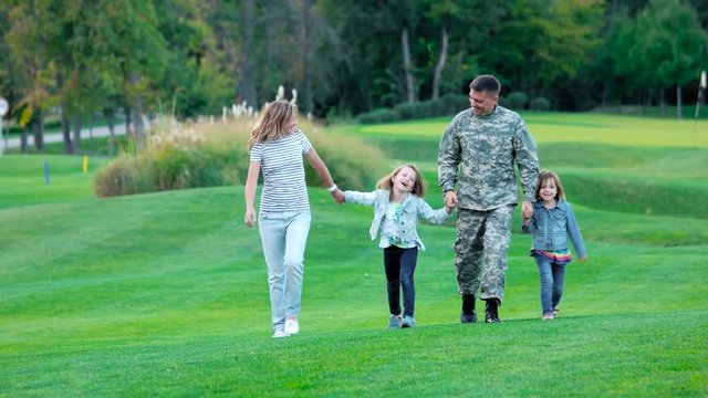 Happy kids and their parents having fun in the summer park. Soldier father with kids and wife walking on lawn.