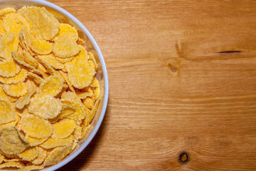 Top view on a portion of a bowl with yellow crispy cornflakes close-up on a wooden table. Copy space.