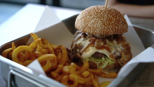 Melted cheese on beef burger with onion and curly fries serve in tray