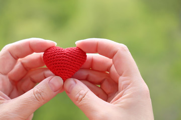Red knitted heart in female hands on blurred nature background. Concept of love, romance, health...