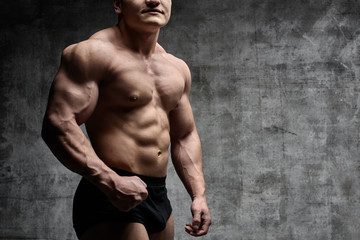 Sexy bodybuilder man posing on dark background in black shorts. Handsome pumped male body isolated with free space for advertising