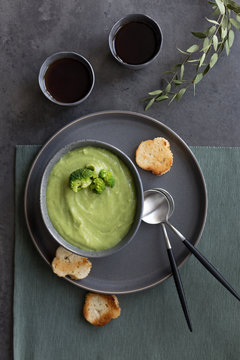 Broccoli soup with bread and spoon on gray background