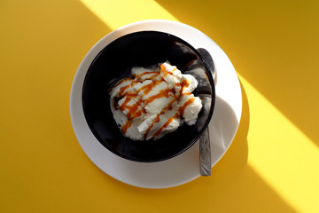 Vanilla ice cream in black bowl on yellow background