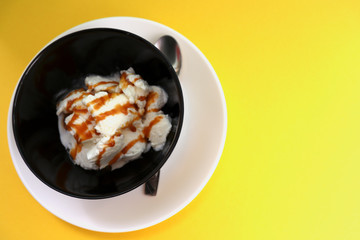 Vanilla ice cream in black bowl on yellow background